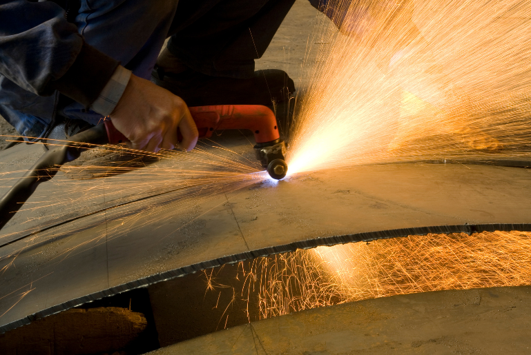 Worker using an angle grinder on metal, sending bright orange sparks across the surface