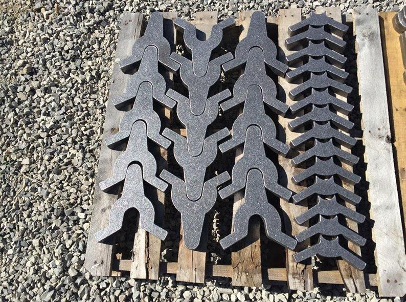 Three black rubber traction mats stacked on a wooden pallet over gravel