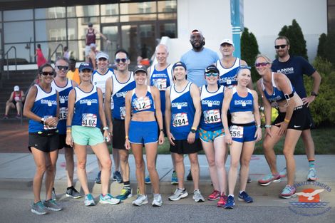 A group of runners are posing for a picture in front of a building.