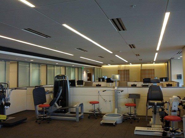 Exercise equipment in a modern, well-lit physical therapy room with workstations visible in the background.