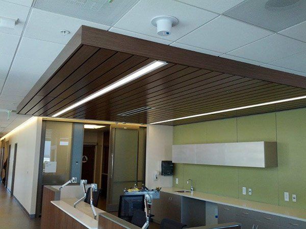 Office ceiling with brown wood paneling and recessed lighting, over a workspace.