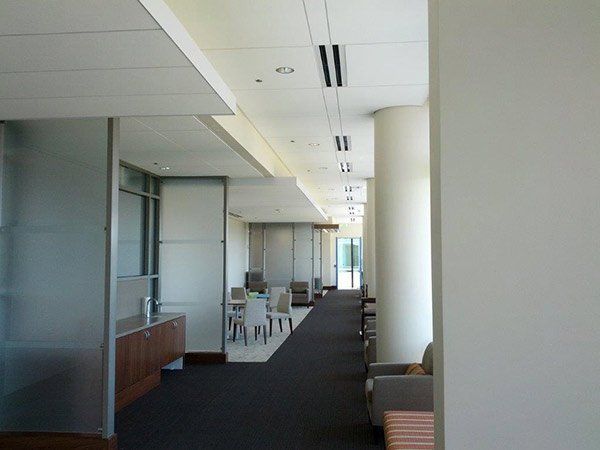 Interior of a modern office hallway with frosted glass walls, dark carpet, and neutral-colored furniture.