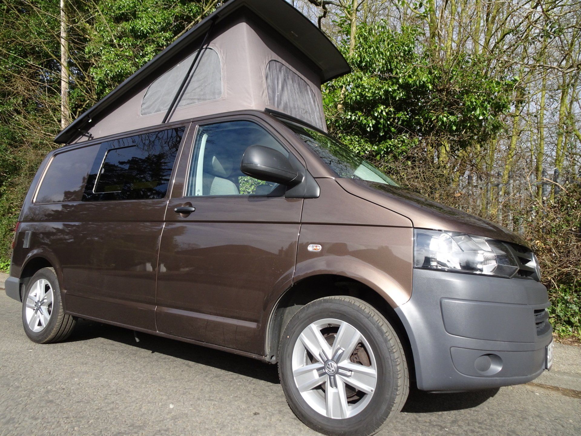 A brown van with a pop top roof is parked on the side of the road.