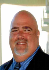 A bald man with a beard is wearing a suit and tie and smiling.