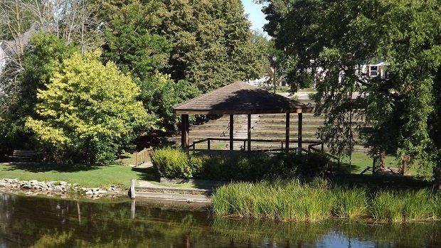 A gazebo is sitting on a small island in the middle of a lake surrounded by trees.
