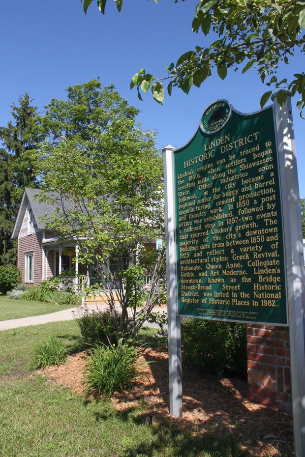 Green historical marker in front of a house. Sunny day with trees and a clear blue sky.