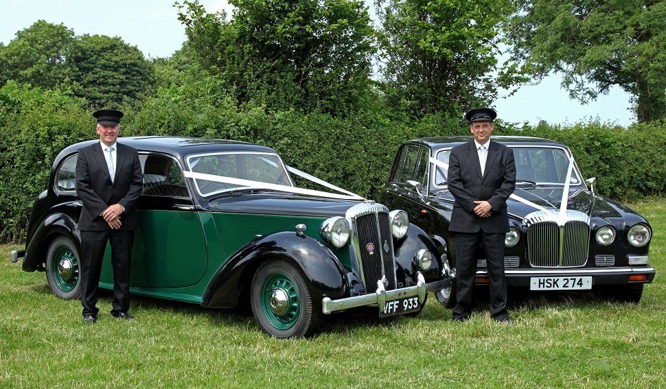 Two chauffeurs next to one green and black wedding car, and one black one