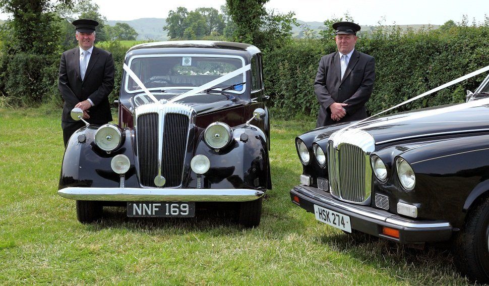 Two chauffeurs next to classic wedding cars