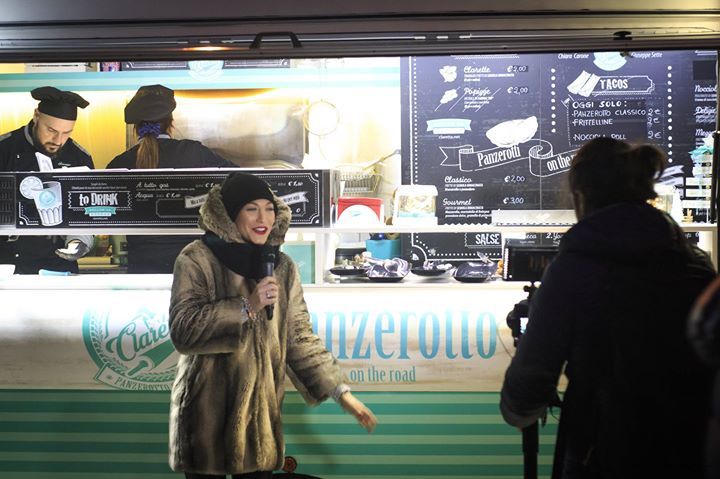 Una donna è in piedi davanti a un camioncino che vende cibo e tiene in mano un microfono.