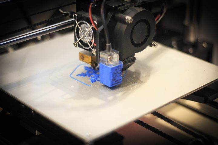 Una stampante 3D stampa un oggetto blu su una superficie bianca.