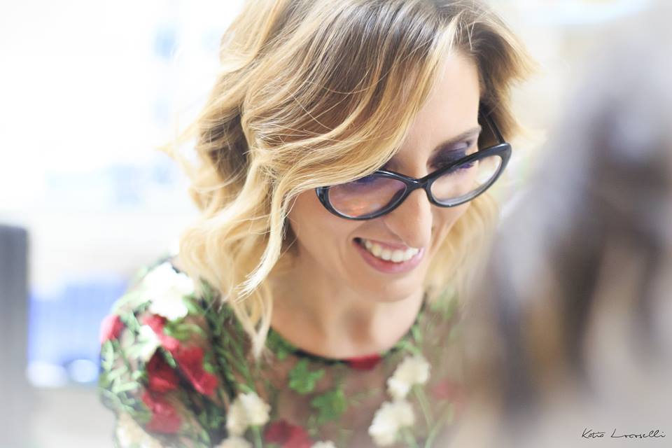 Una donna che indossa occhiali e una camicia a fiori sorride.