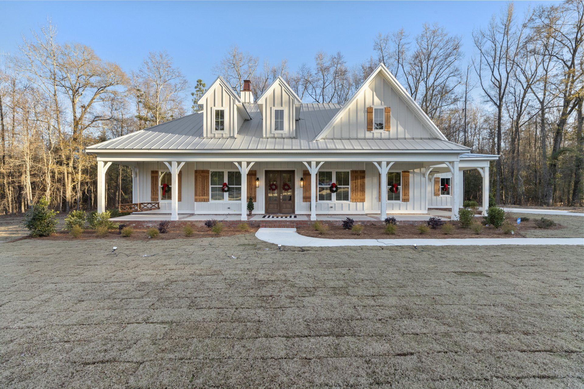 Large cream-colored house with a wraparound porch, dormer windows, and a wide gravel yard in front.