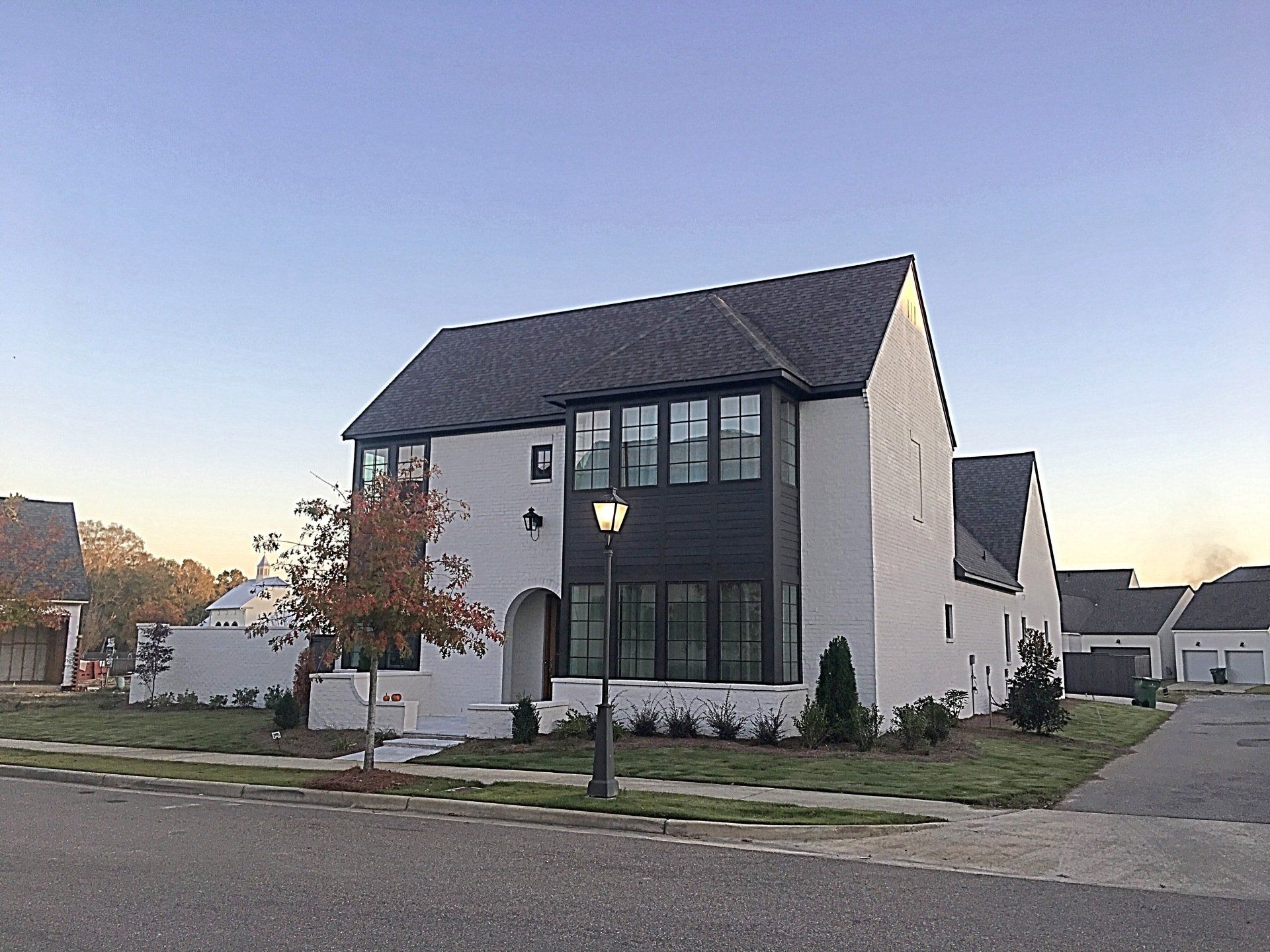 Modern white two-story house with black roof and large front windows at dusk