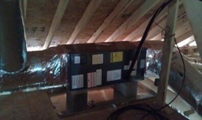Small black control panel mounted under a slanted wooden ceiling with wires and foil insulation nearby.