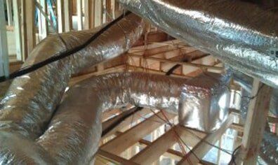 Silver HVAC ducts and wooden roof framing inside an unfinished attic.