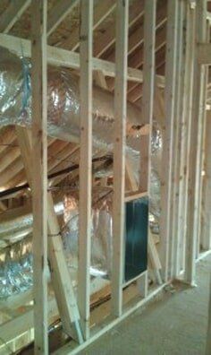Unfinished house interior with exposed wooden framing, insulation, and a concrete floor.