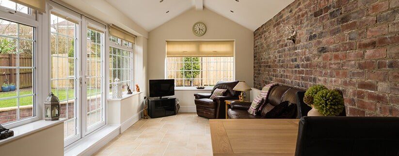 Bright sunroom with large windows, brick accent wall, beige carpet, and dark furniture seating area