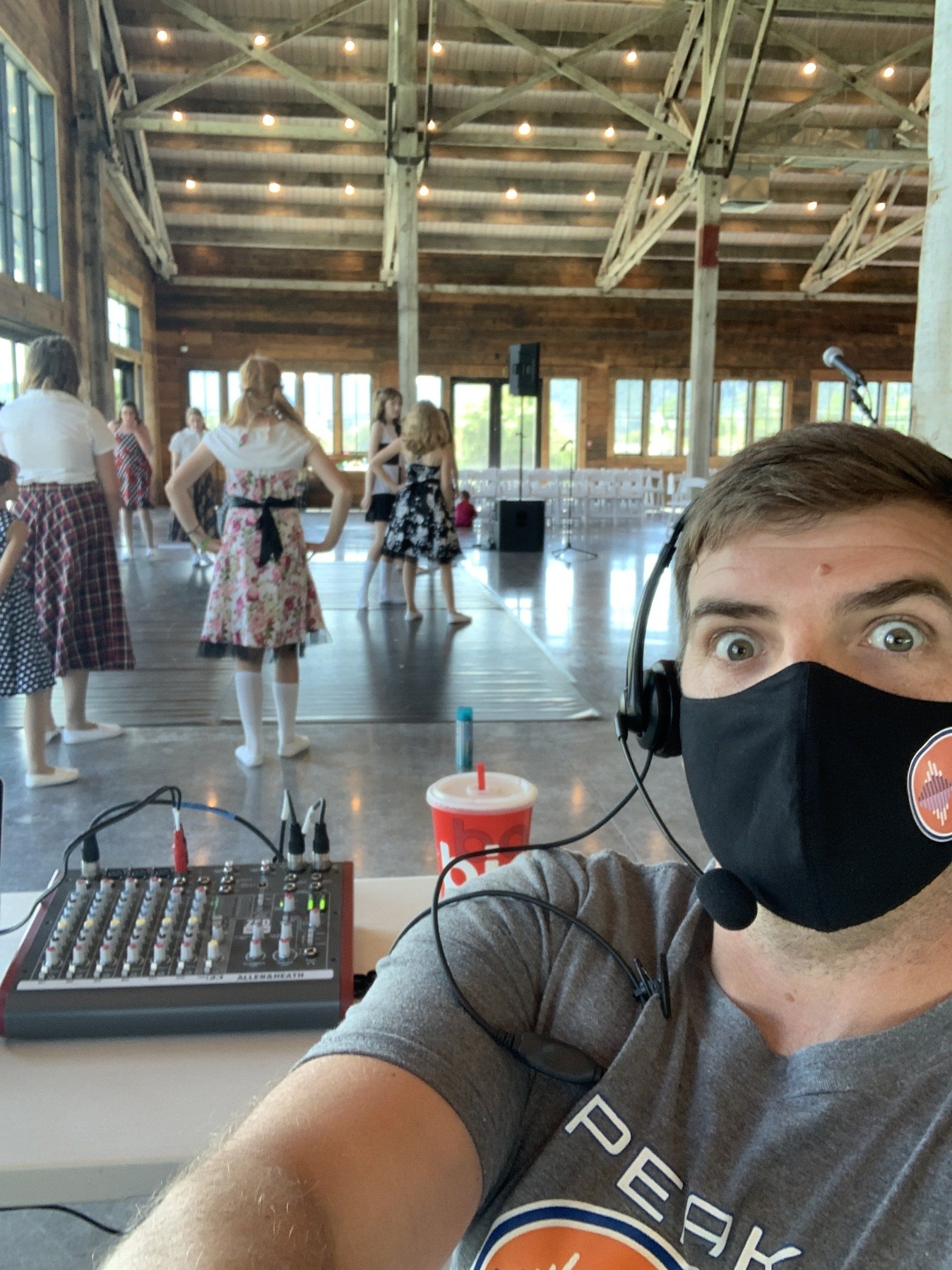 A man wearing a mask and headphones is taking a selfie in a large room.