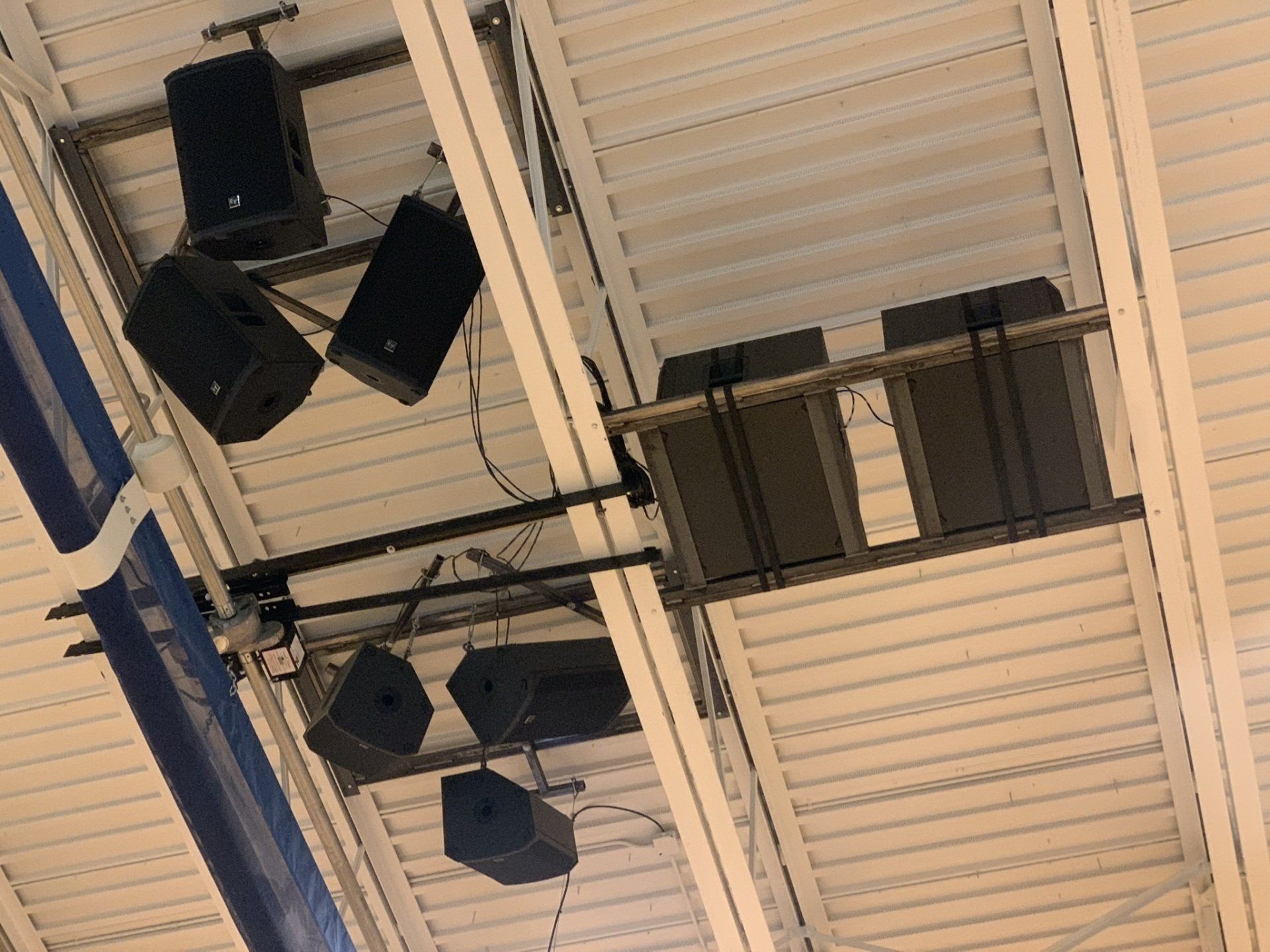A bunch of speakers are hanging from the ceiling of a building