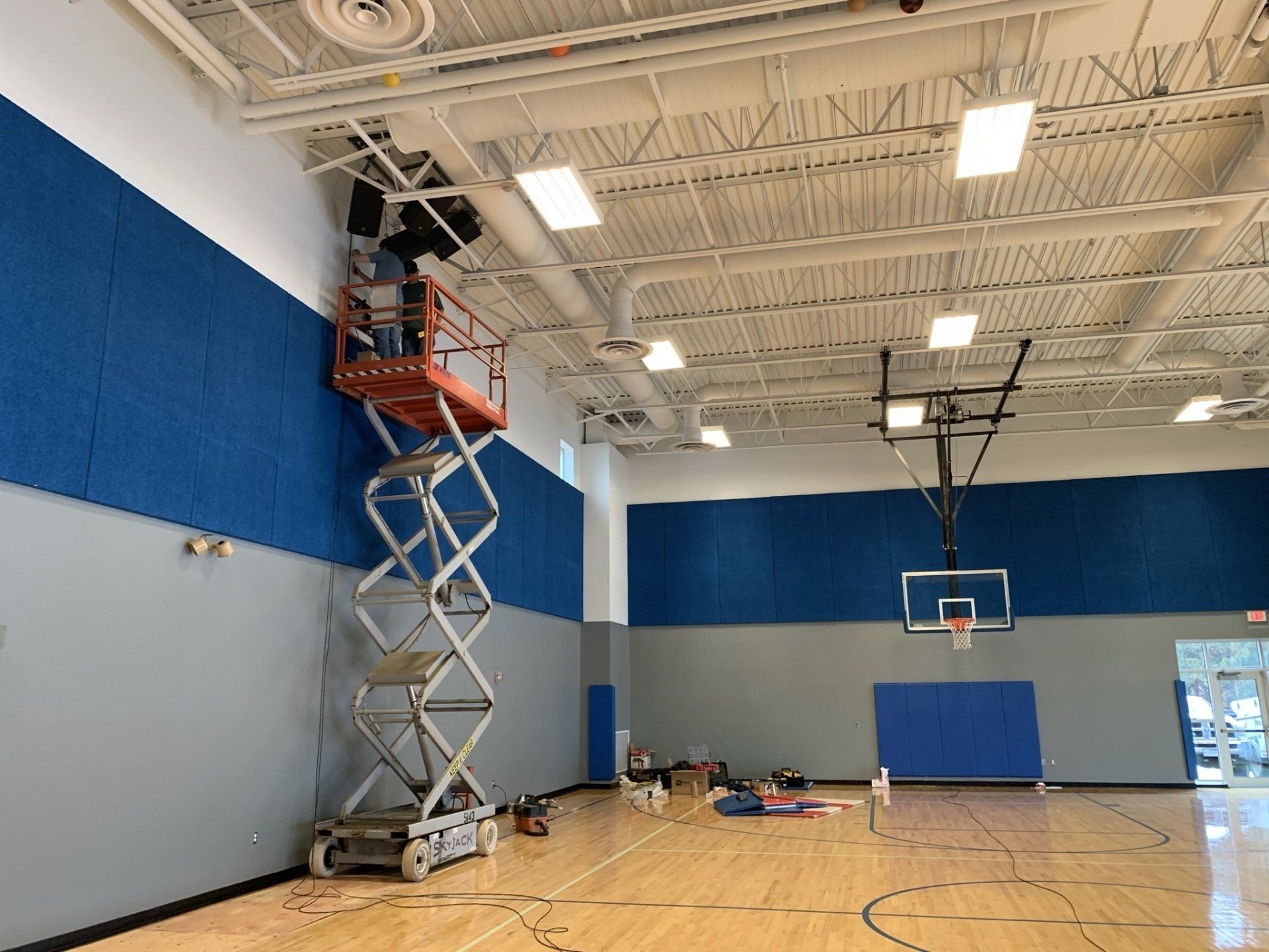 A man is standing on a scissor lift in a gym.