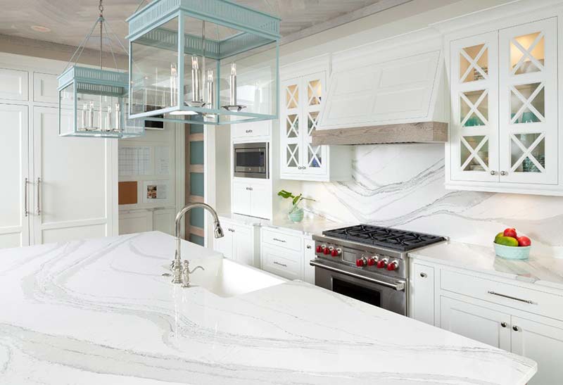 White kitchen with marble countertops, stainless steel appliances, and blue light fixtures.