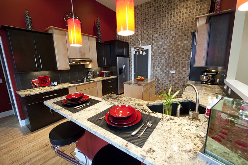 Modern kitchen with red walls, dark cabinets, granite countertops, and two orange pendant lights.