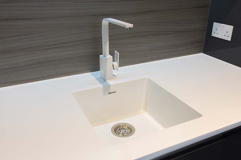 White kitchen sink with faucet against a wood-grain backsplash and white countertop.