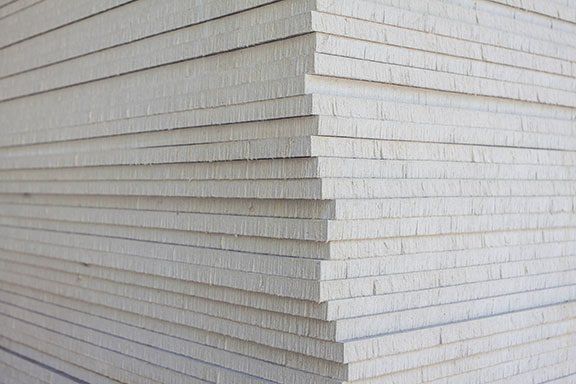 Stack of drywall sheets, light gray, stacked at a corner, ready for construction.