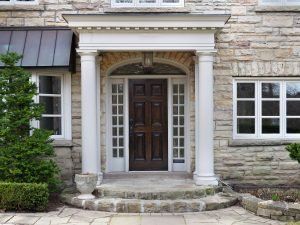 Stone house entrance with columns, arched doorway, and wooden door.
