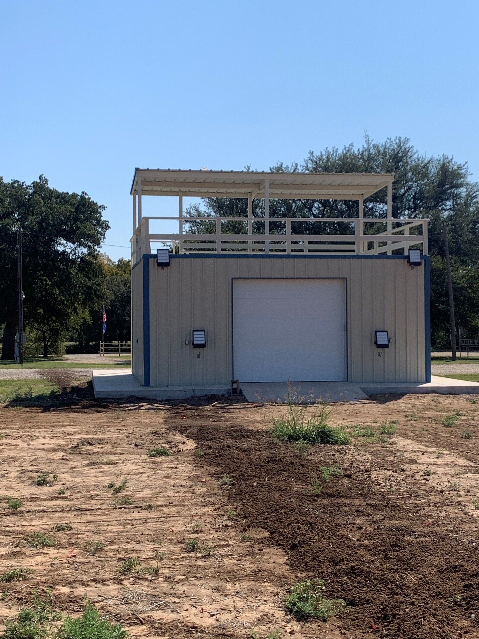 A building with a white garage door is in the middle of a field