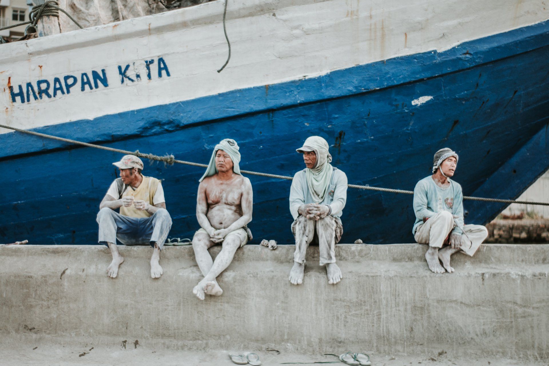 Photo by vjapratama A group of people are sitting on a wall in front of a boat.