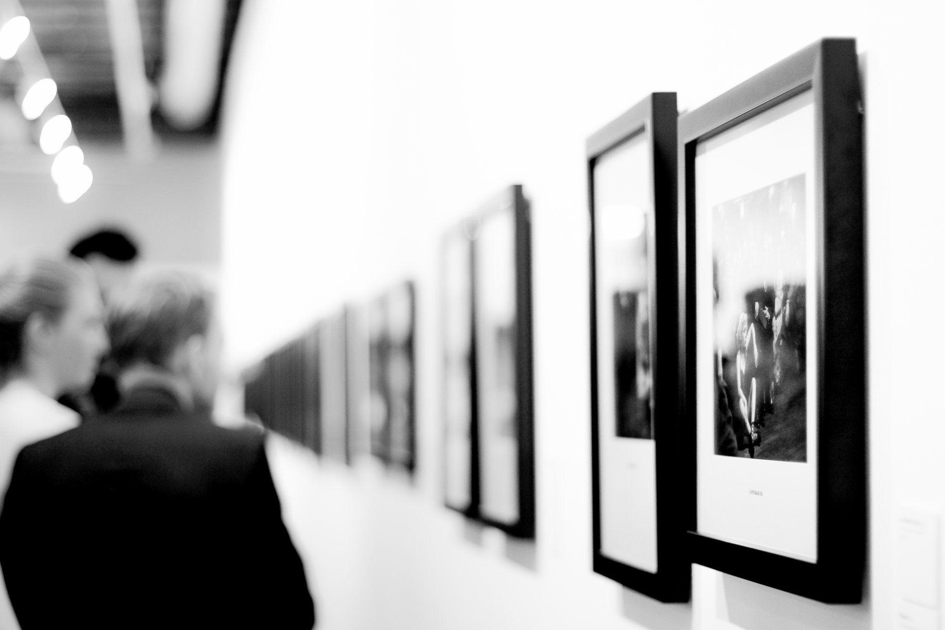 Photo by Adrianna Calvo A black and white photo of people looking at pictures on a wall.