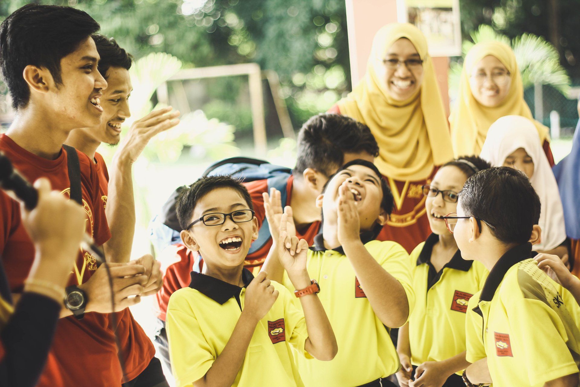 Photo by Iqwan Alif A group of children in yellow shirts are standing next to each other and laughing.