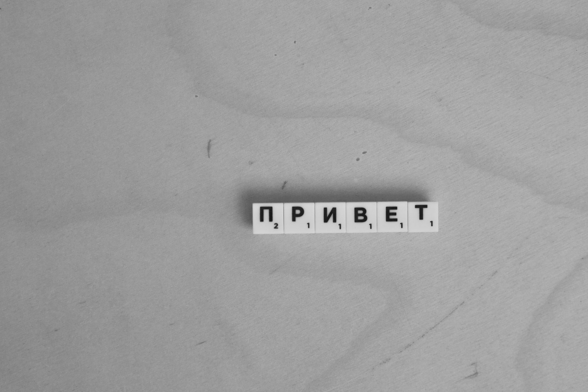 A black and white photo of a scrabble board with the words `` привет '' written on it.
