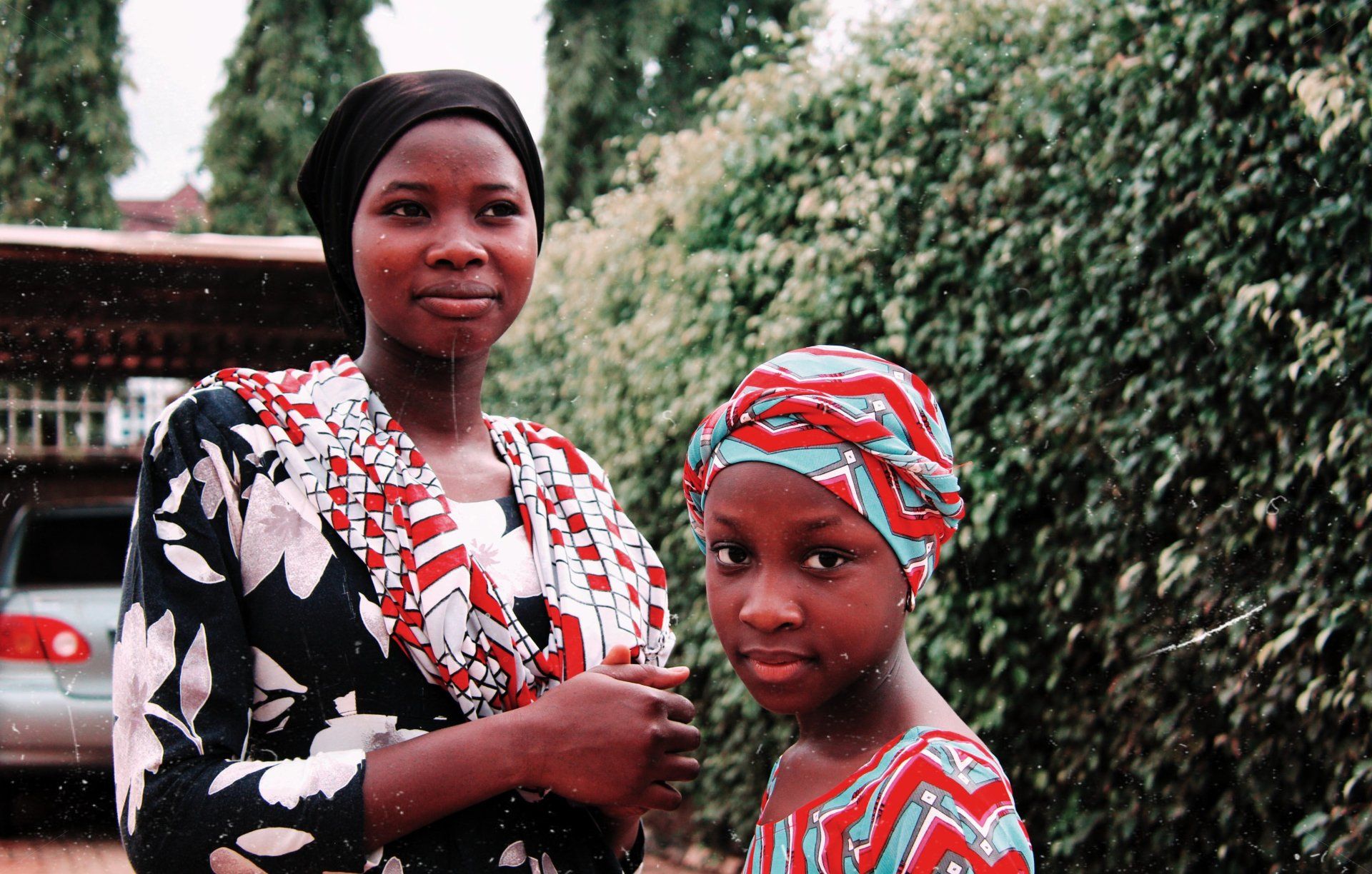 Photo by Muhammadtaha Ibrahim Ma'aji A woman and a little girl are standing next to each other in front of a bush.