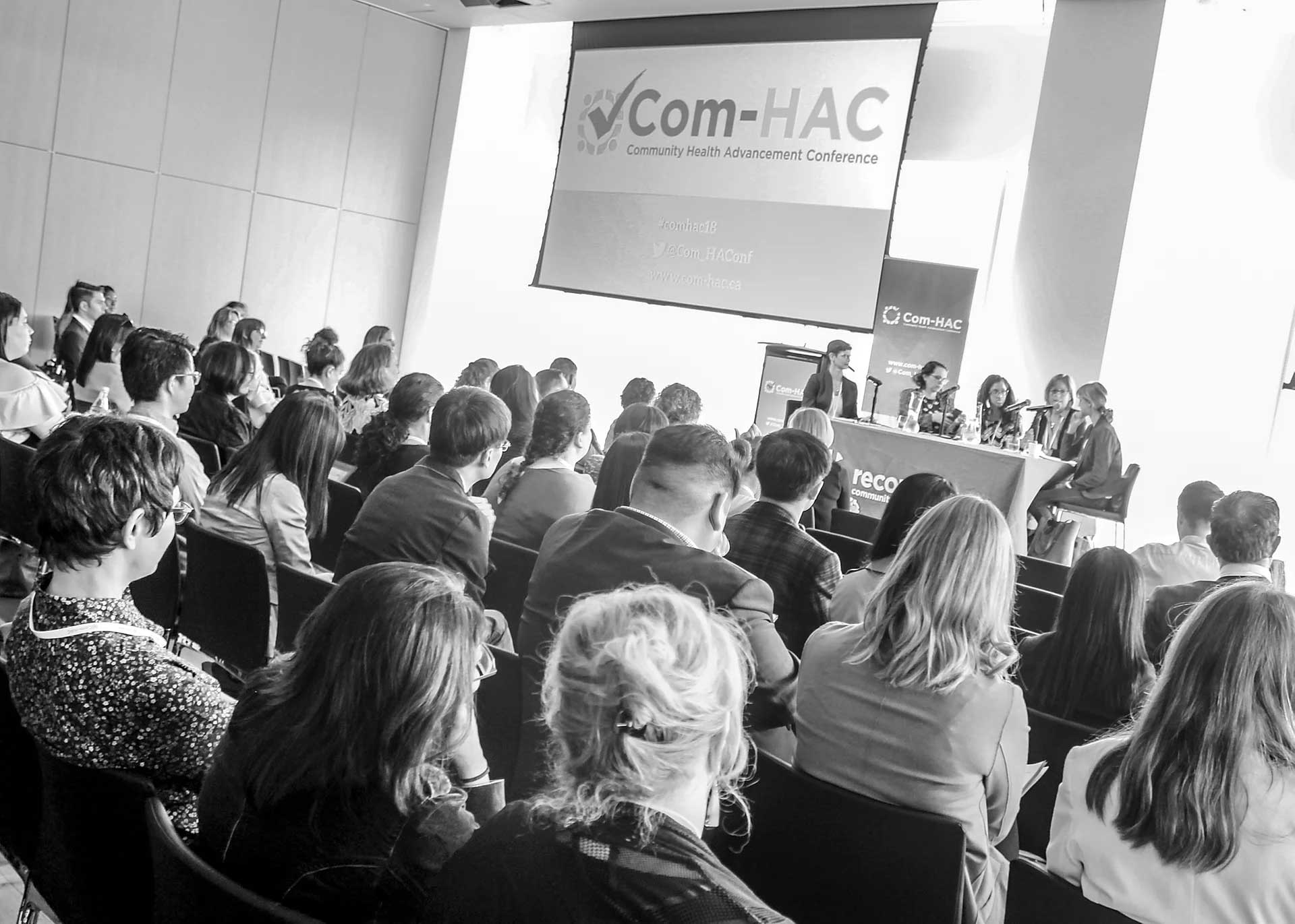 A group of people are sitting in front of a screen that says com-hac.