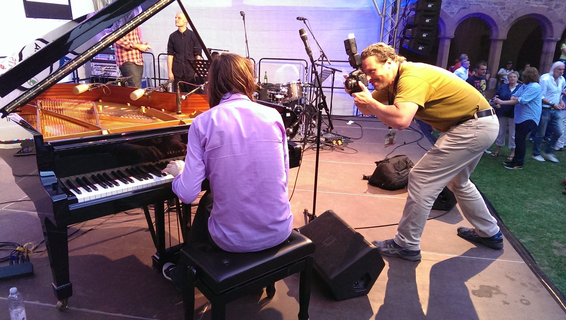 Musiker treten auf der Bühne auf, ein Pianist sitzt an einem Flügel und ein Fotograf kauert in der Nähe.
