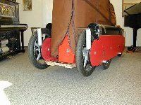 Ein roter Elektromobil, von hinten in einem Innenraum gesehen, mit großen schwarzen Rädern und einem braunen Sitzbezug.
