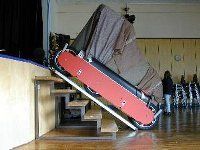 Person trägt ein rot-schwarzes Skateboard eine Holztreppe in einem Gebäude hinauf