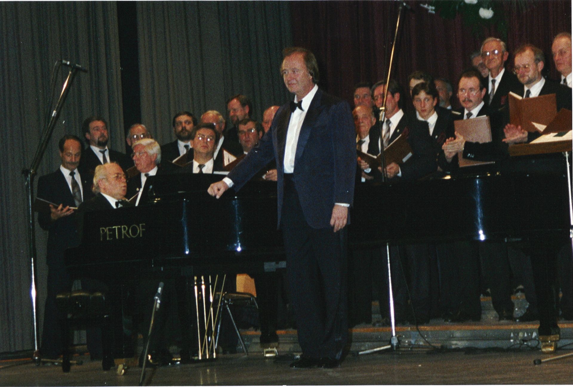 Ein Chor tritt mit einem Pianisten im Smoking unter warmem Bühnenlicht auf.