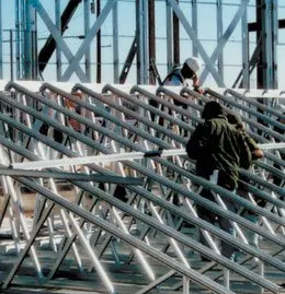 Construction workers on a roof assembling metal trusses.