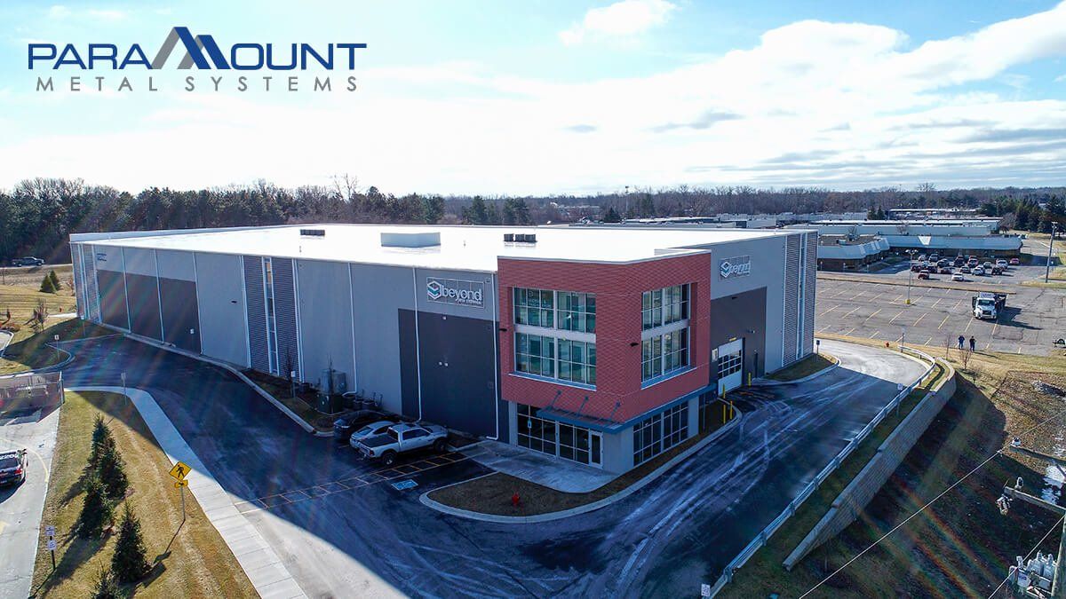 Aerial view of Paramount Metal Systems building: gray and red exterior with blue sky.