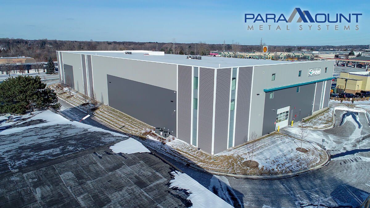Aerial view of a gray industrial building with a Paramount Metal Systems logo on a snowy day.