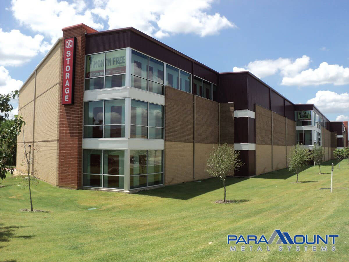 Storage facility building with brown and tan exterior, glass windows, and green lawn.