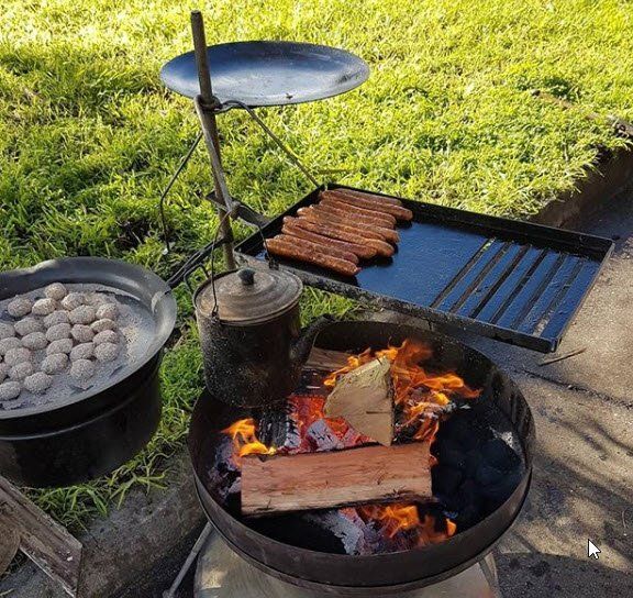 A tray of sausages is cooking over a fire