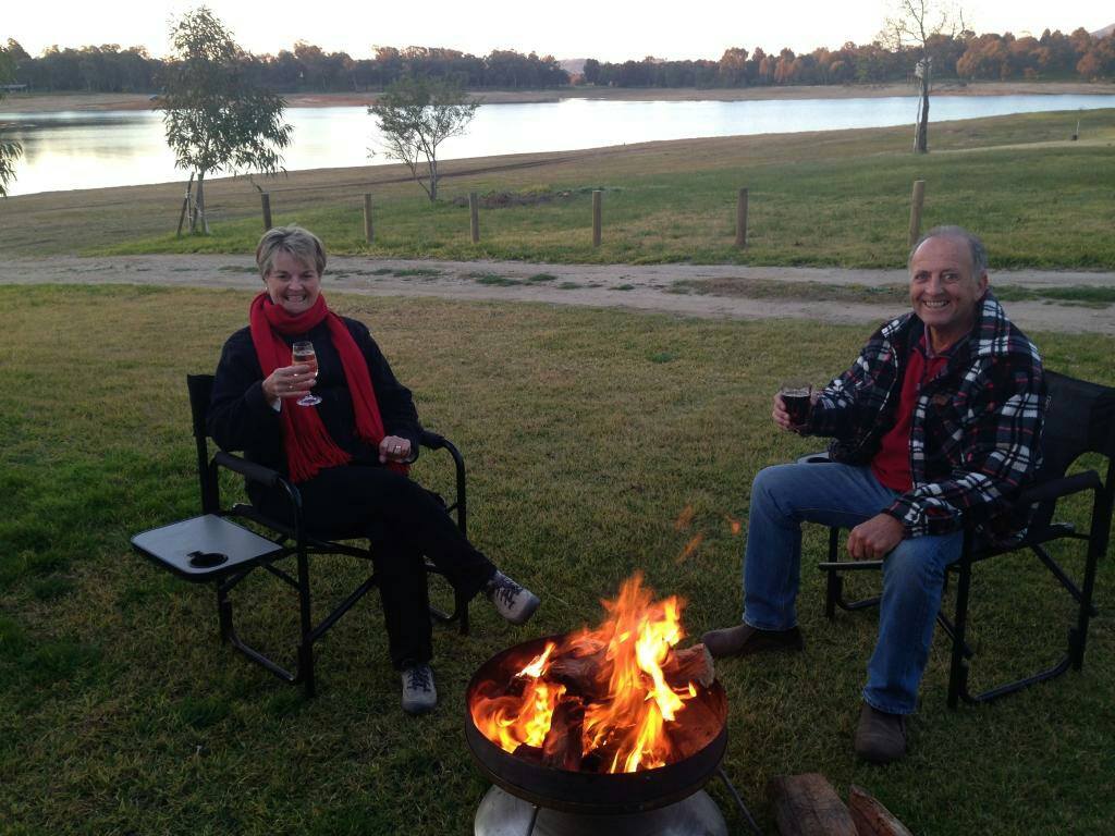 A man and a woman are sitting around a fire pit drinking wine.