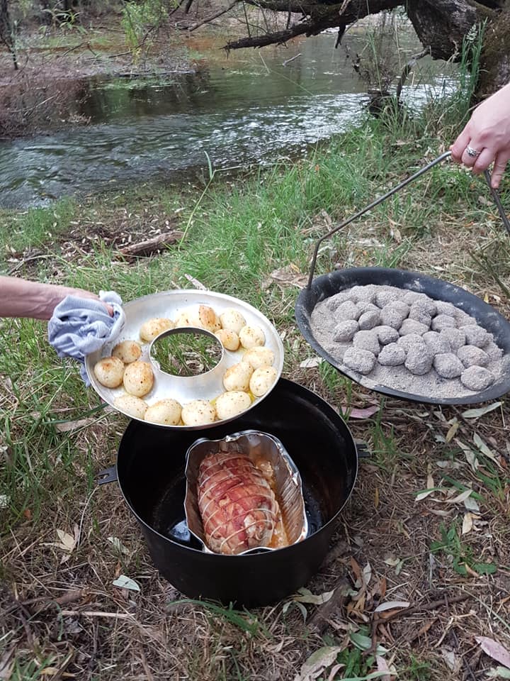 A person is cooking food in a dutch oven in the woods.