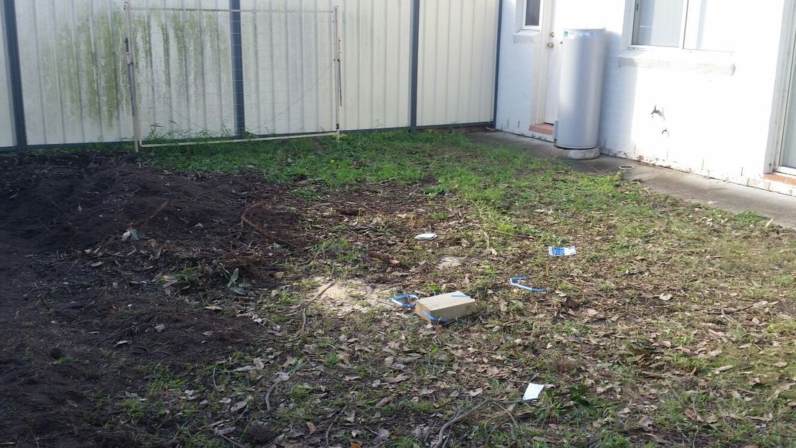 A backyard with a white fence and a brick in the grass.