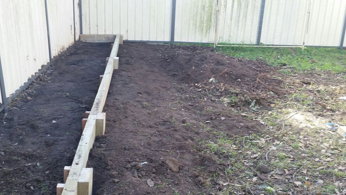 A backyard with a fence and a pile of dirt.