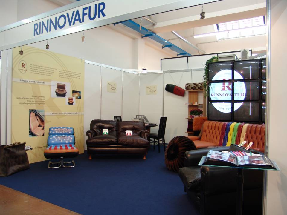 Stand fieristico per RINNOVAFUR con esposizione di mobili su un pavimento ricoperto di moquette blu.